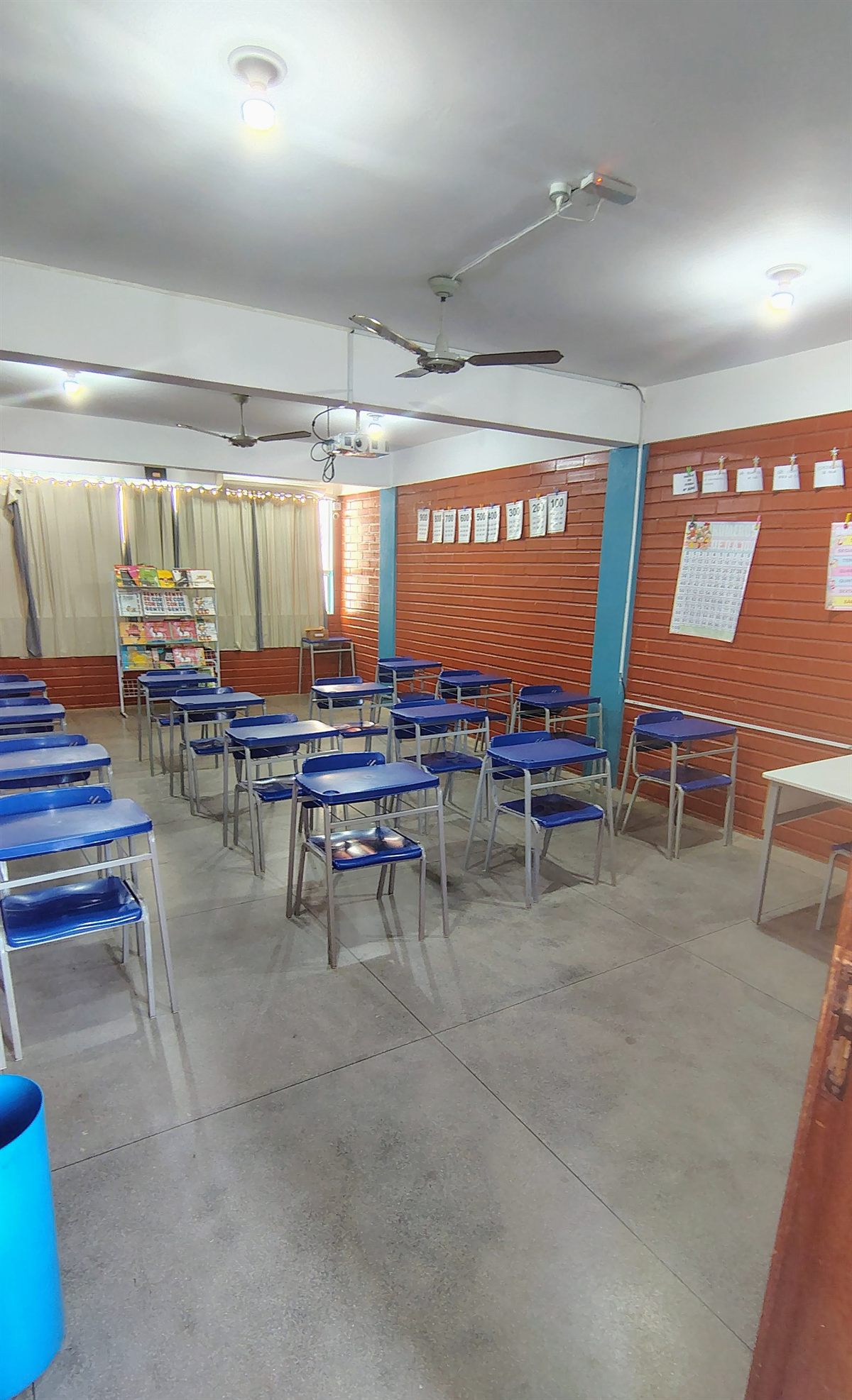 Sala de aula com carteiras azuis e cantinho de livros